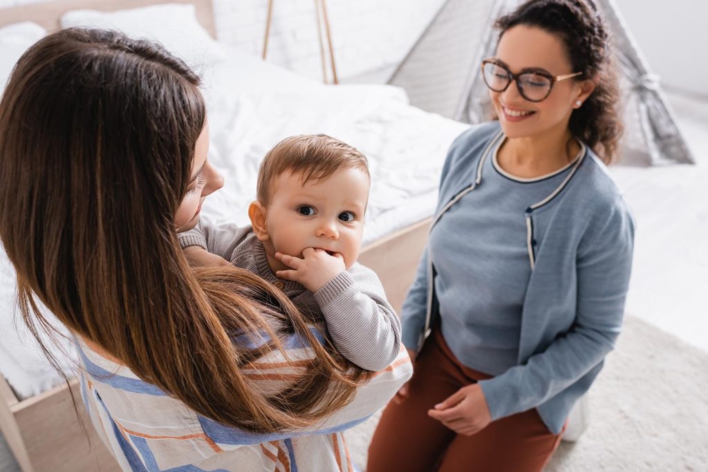 A young mother holding her baby while her friend is smiling